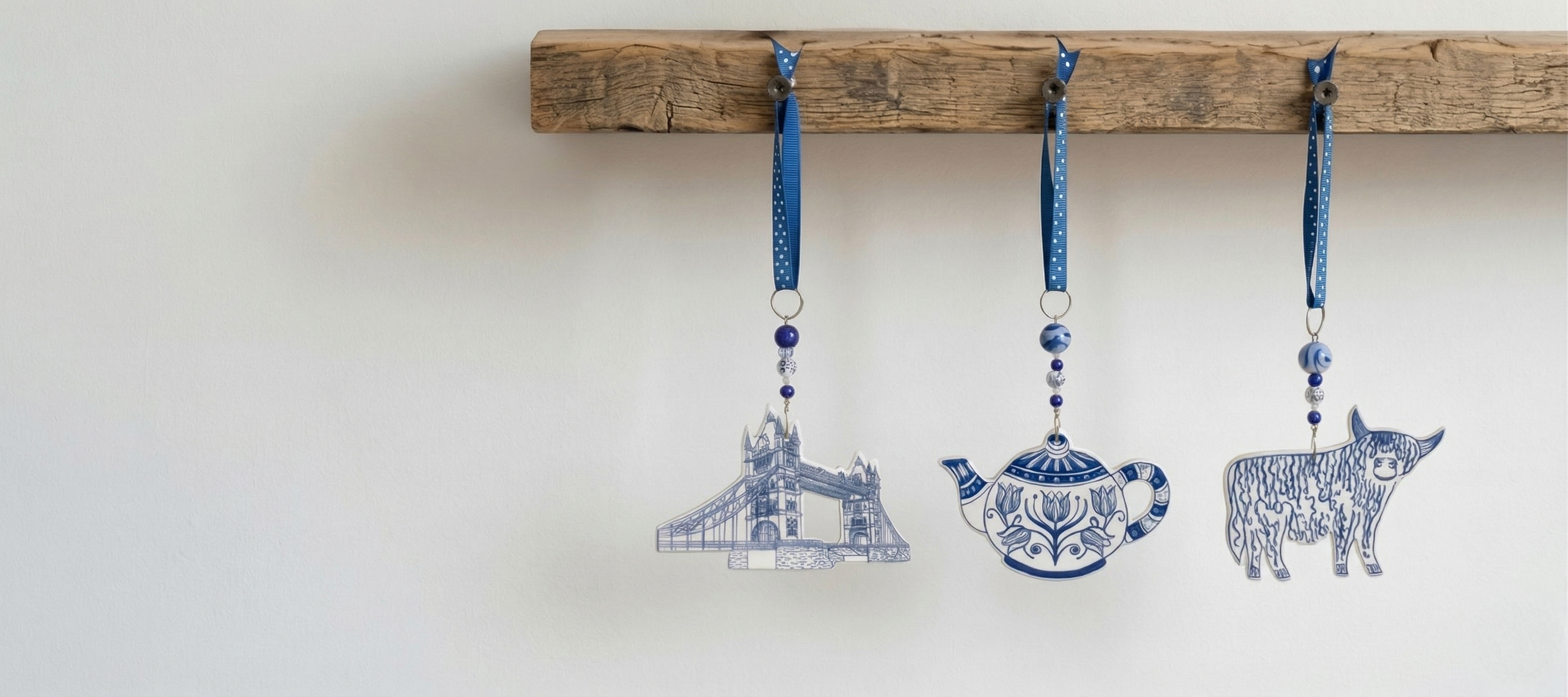 Handmade ceramic decorations — Tower Bridge, teapot and highland cow — hanging from a wooden peg rail